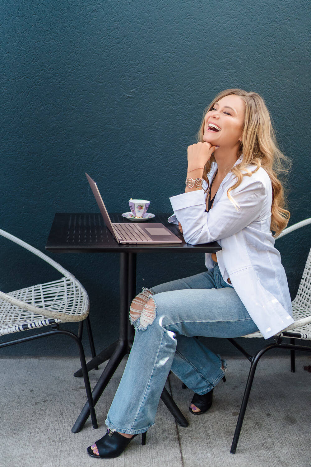 Entrepreneur sitting at outdoor Kelowna café table with coffee, laptop open, looking thoughtful.