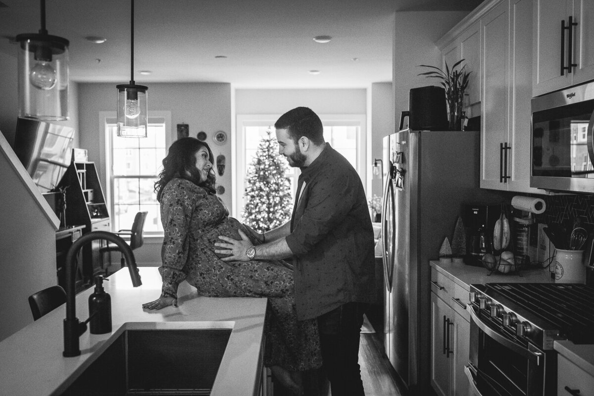 Pregnant woman sitting on counter with partner standing in front of her