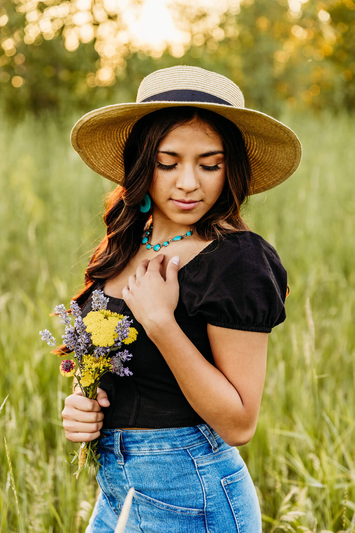 stunning teen girl in a sun hat holding a bouquet and glancing down as she touches her necklace in a beautiful nature scene near Appleton WI