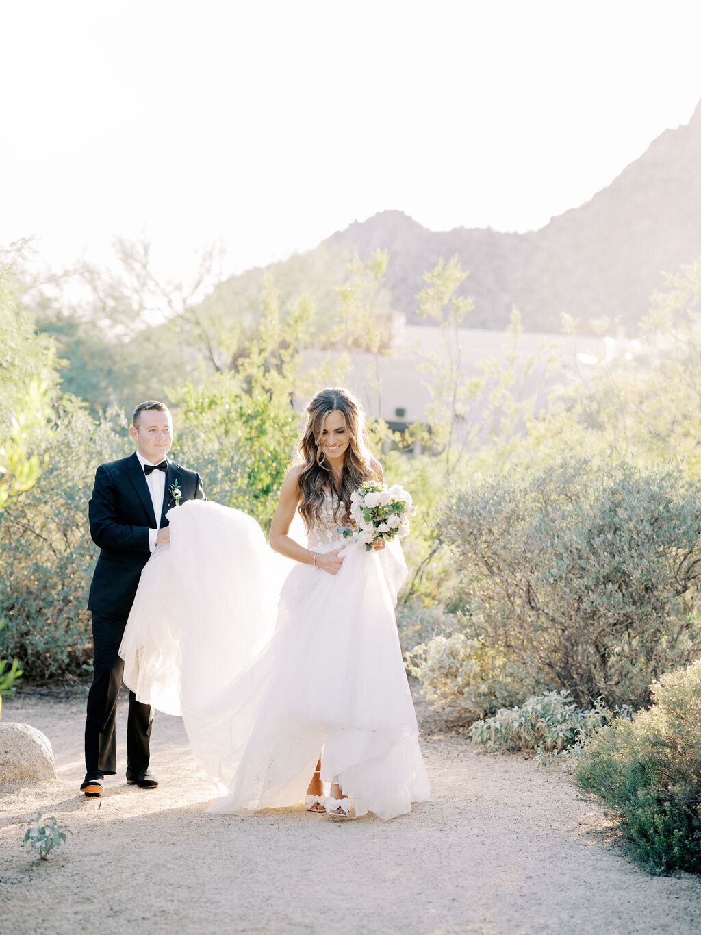A newlywed couple takes a romantic stroll through the desert landscape, capturing the essence of love and elegance on their wedding day.