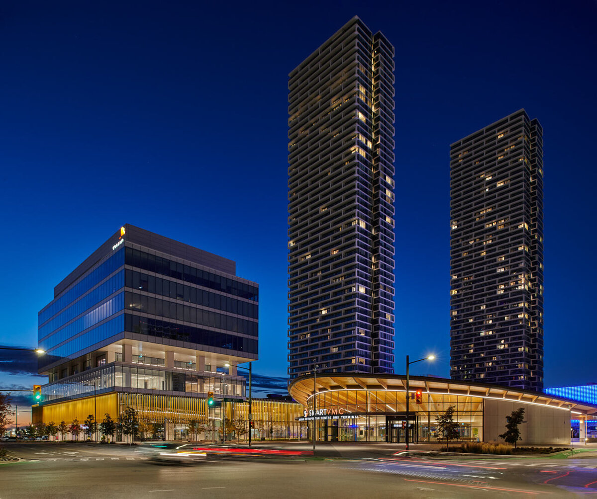 A nighttime architectural photograph of SmartCentres VMC in Vaughan, Ontario, designed by Diamond Schmitt Architects. The image showcases illuminated high-rise towers, a modern glass office building, and the Vaughan Metropolitan Centre transit hub. Captured by Brandon Marsh Photo & Video Productions, highlighting contemporary urban design and city life.