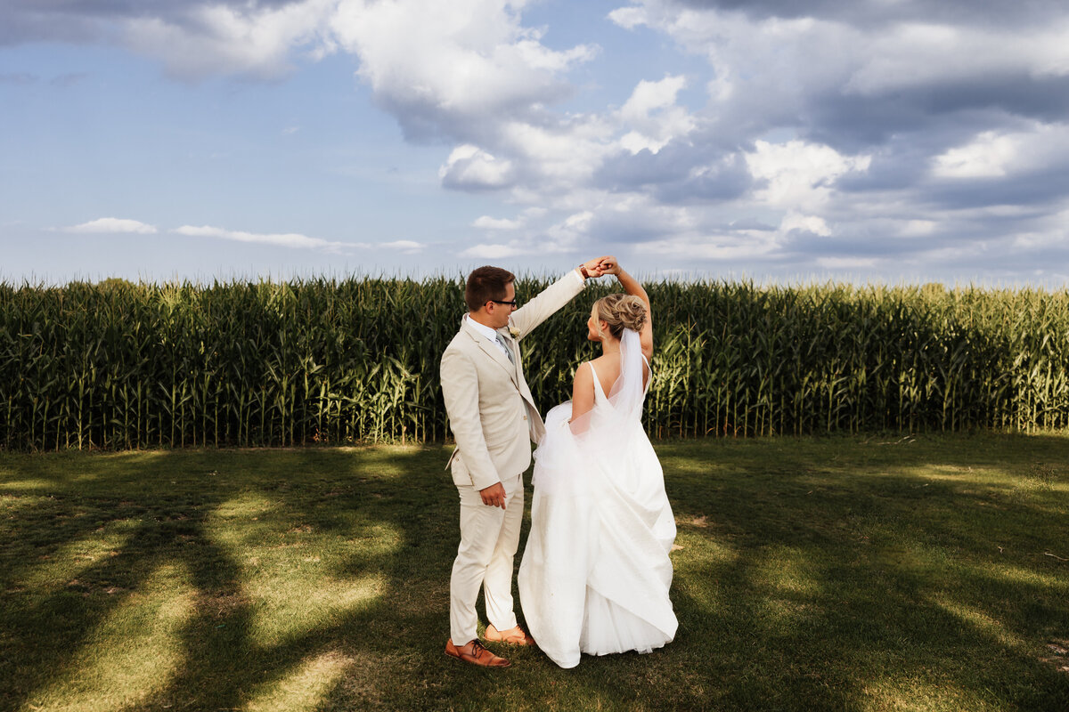 A wedding couple twirls in front of a cornfield.