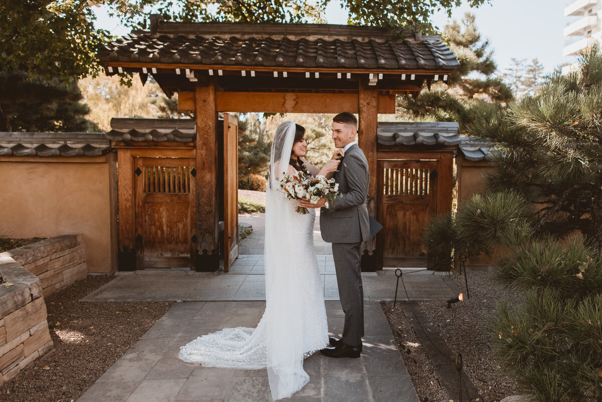 Bride and groom adjust his grey tuxedo on their wedding day.