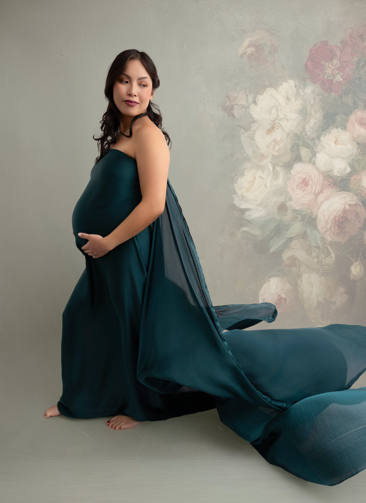 Pregnant mother wearing green silk fabric tossed in the air and posed against a light green backdrop.