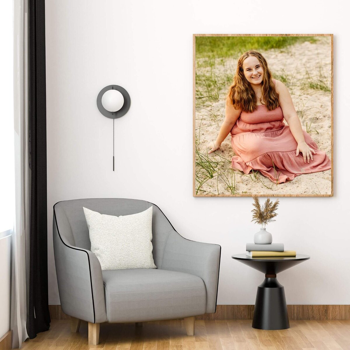 framed image of a senior in a pink dress sitting on a beach hanging on a white wall next to a grey chair.