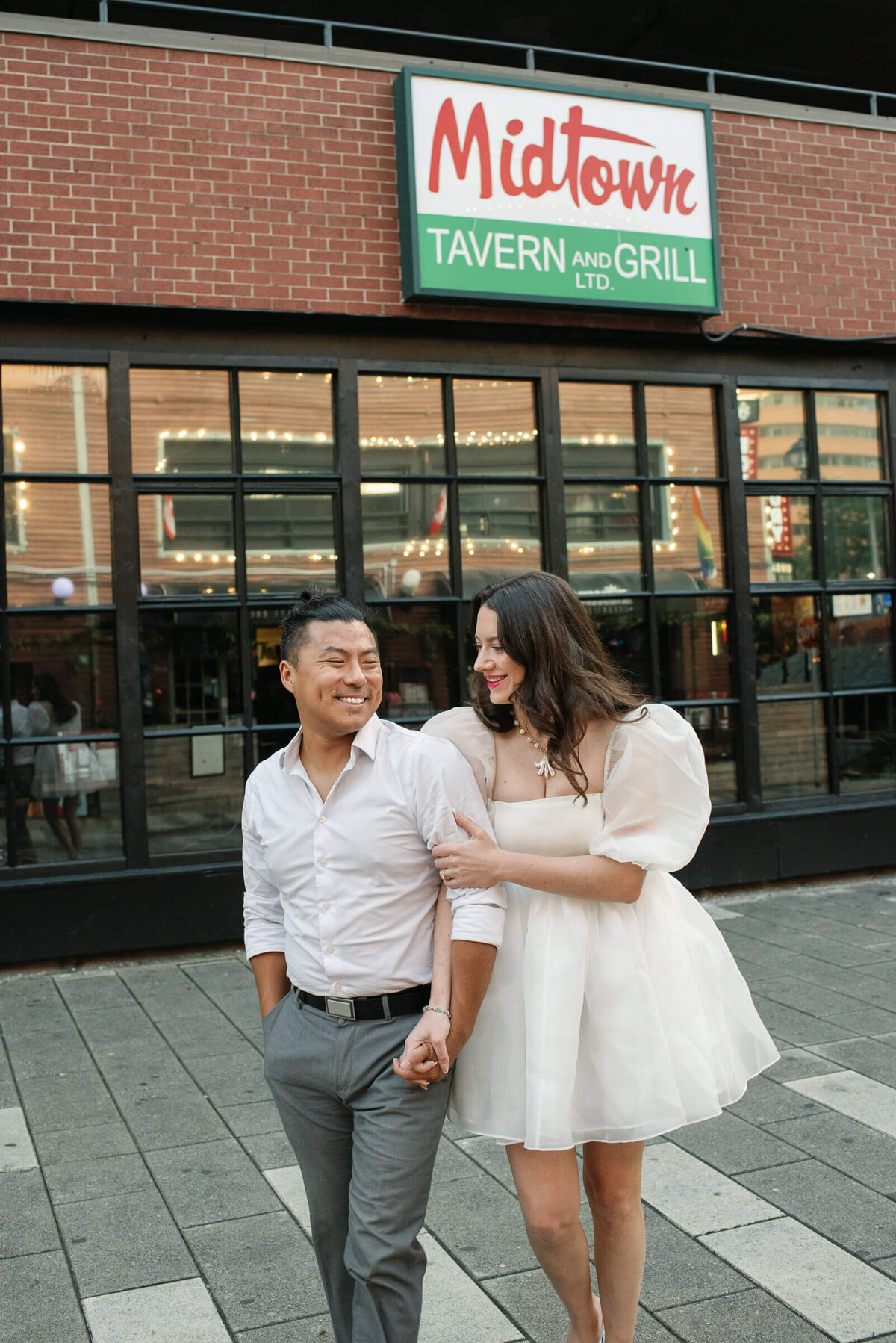 Stylish couple linking arms as they walk past Midtown Tavern in Halifax