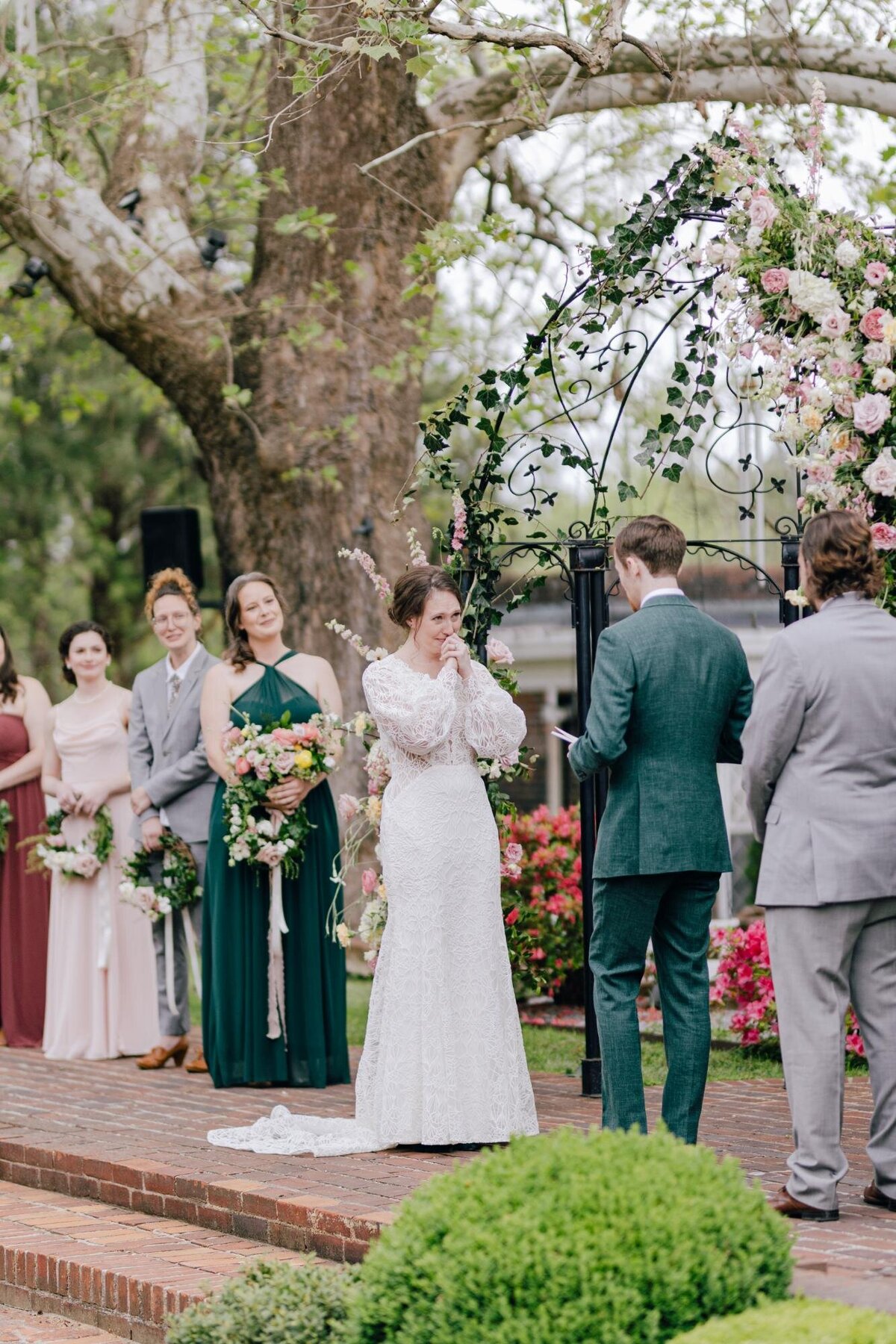 A bride and groom exchange vows at an outdoor wedding ceremony, with bridesmaids and guests watching.