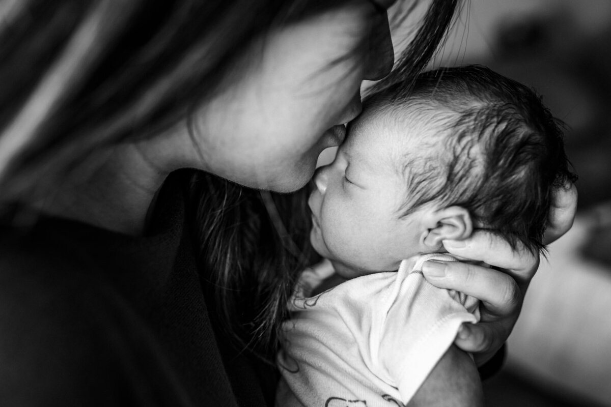 mom holding newborn close to her and kissing baby's forehead