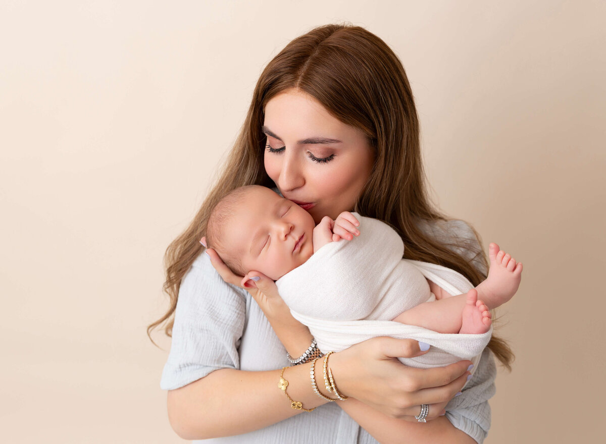 A mother kissing at her newborn with love, captured during a professional Manhattan newborn session