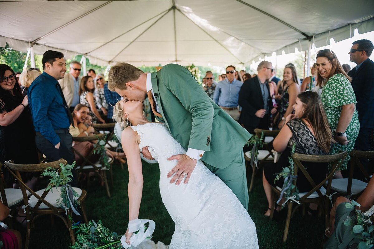 Bride and groom share a kiss surrounded by their guests at the end of their wedding ceremony.