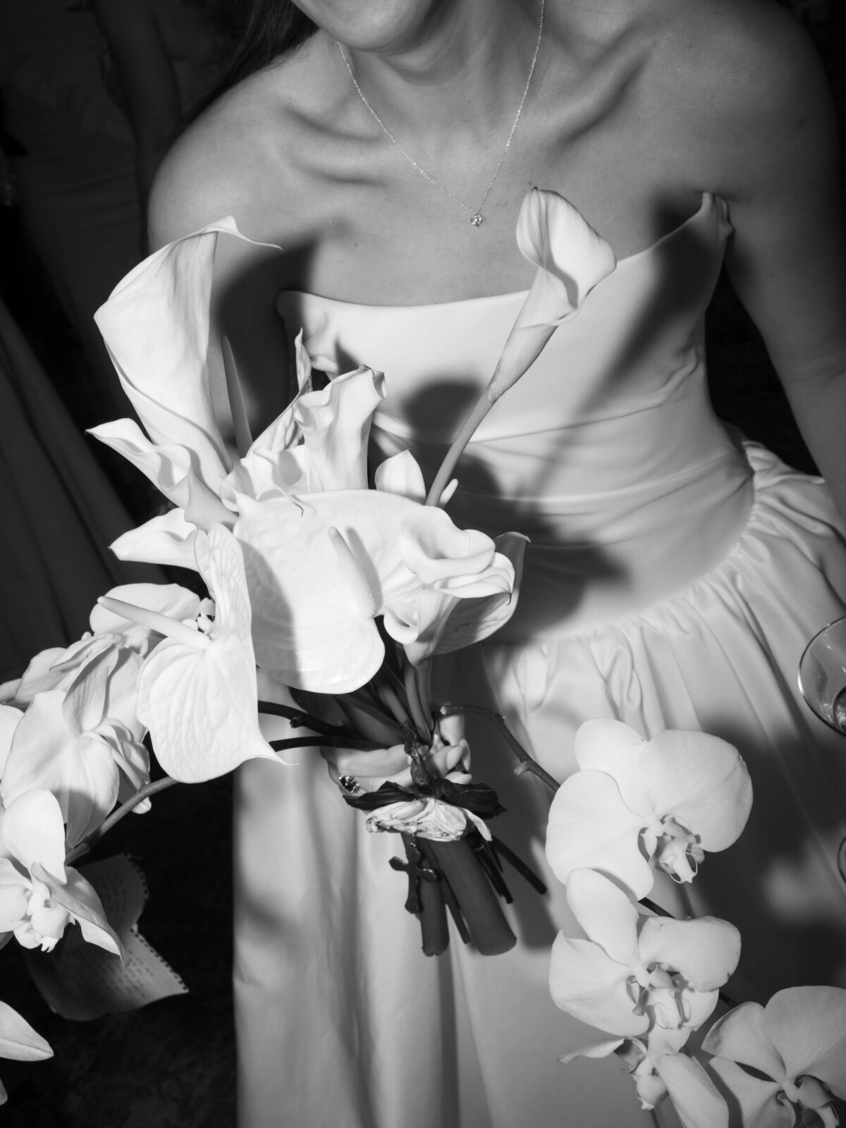 Black and white close-up of bride holding cascading orchid bouquet in strapless wedding gown