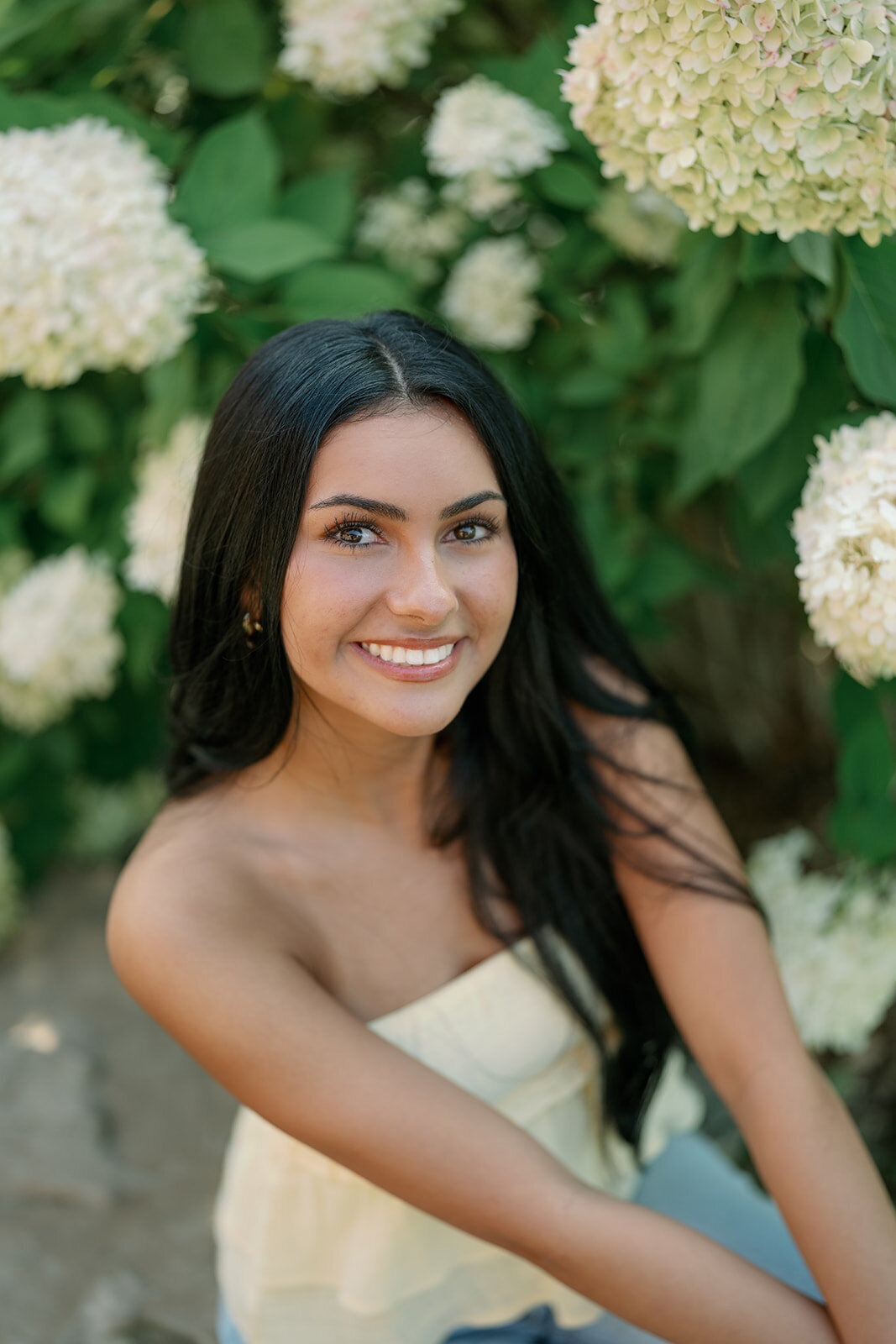 High school senior smiling in front of blooming hydrangeas during her downtown South Haven senior photography session.