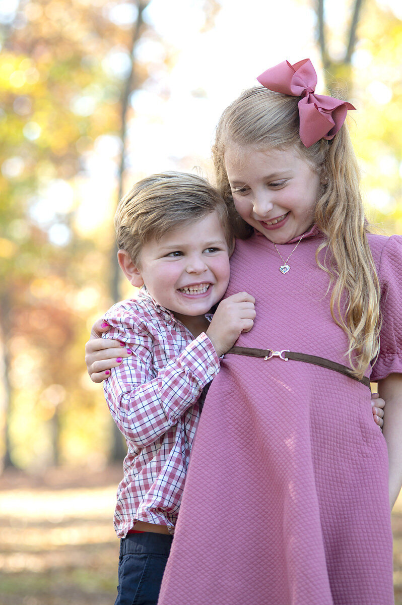 Two small siblings with their arms around each other smiling 