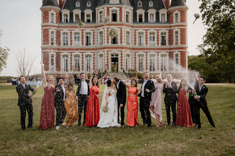 Célébration de mariage festive avec une champagne shower devant un magnifique château en région parisienne, entourés de leurs proches.