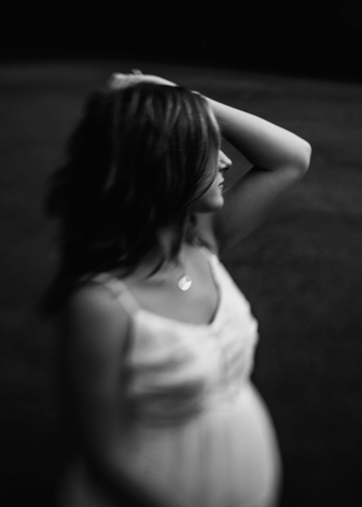 A pregnant woman, dressed in white, stands in the dark as captured by a Pittsburgh maternity photographer.