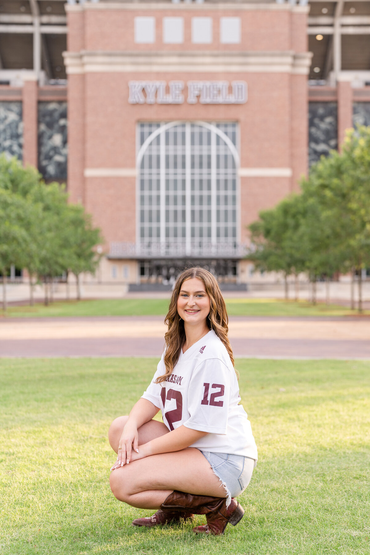 Texas A&M senior girl kneeling down and smiling while wearing Aggie white jersey in Aggie Park