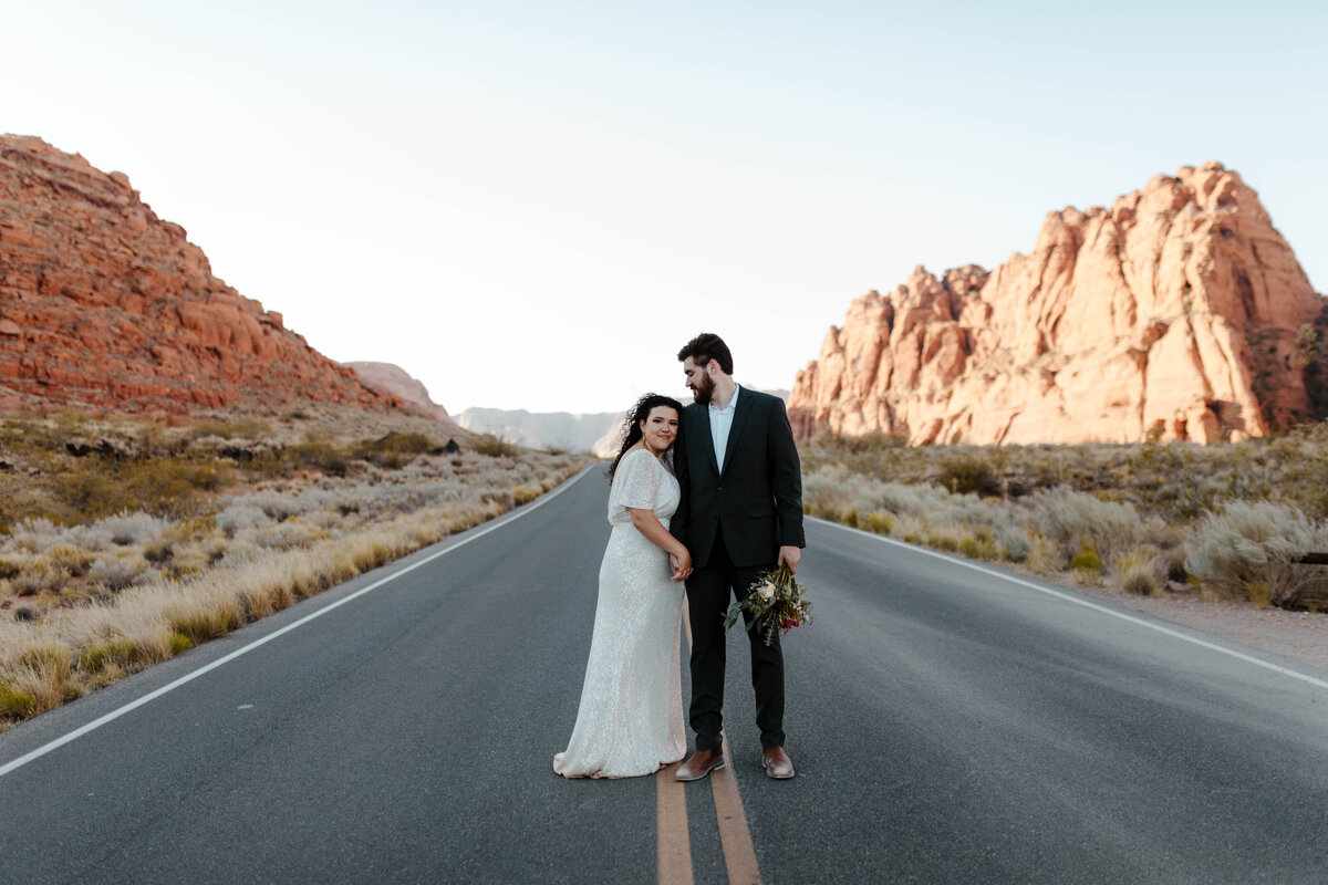 Bride and Groom Standing in Road Surrounded by Red Rocks