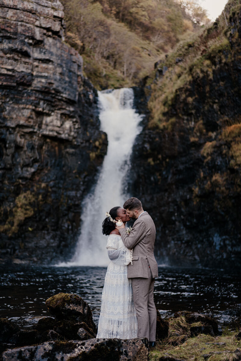 Couple de jeunes mariés enlacés devant une cascade sur l’île de Skye, moment intense au cœur de la nature écossaise.