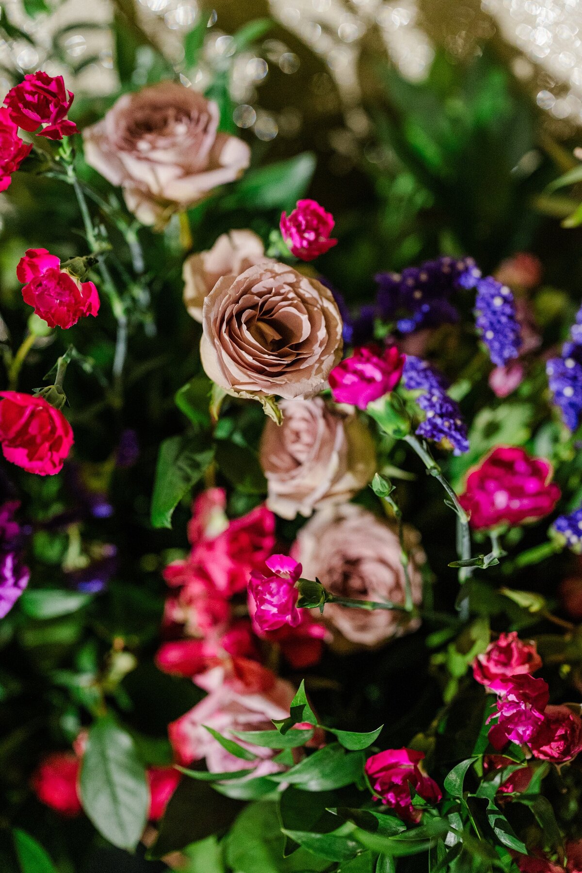 A detail shot of a floral arrangement at a wedding in DFW, Texas. The flowers range from light pink to red to purple and are surrounded by large amounts of greenery.