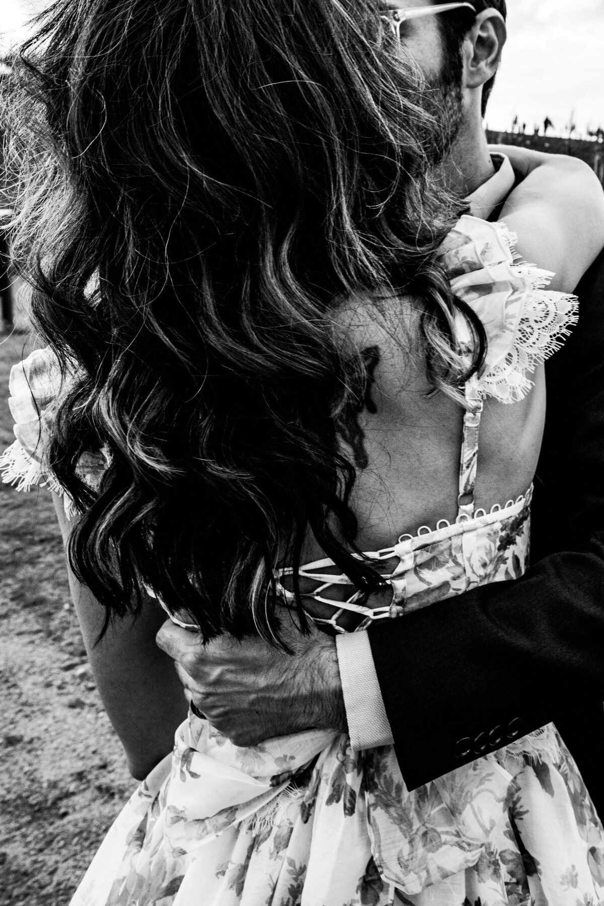 Black and white close-up of a groom embracing his bride, highlighting the intricate lace details of her dress and the intimacy of their moment