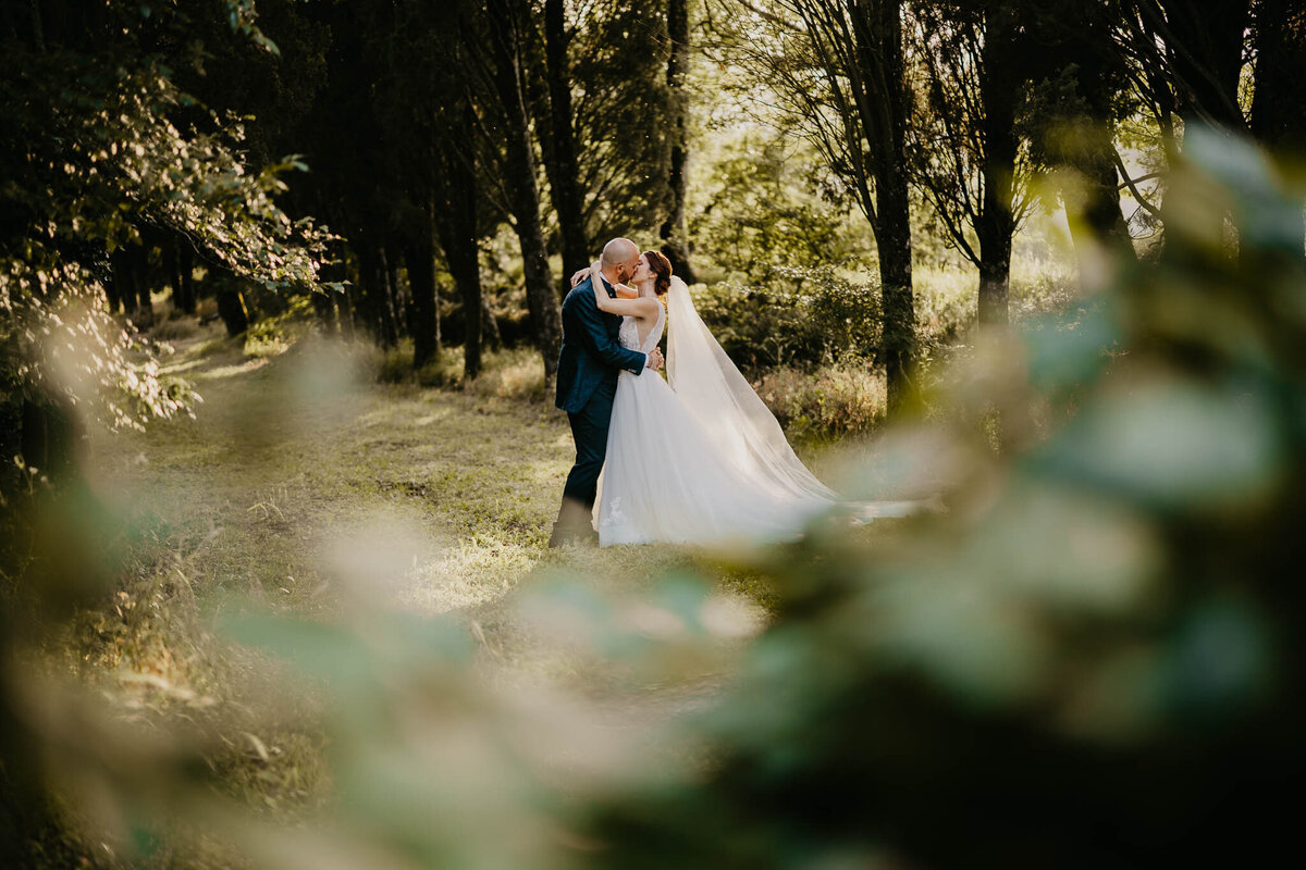 Bride and groom embracing in tree-lined park of villa Bivigliano, wedding photographer Tuscany.