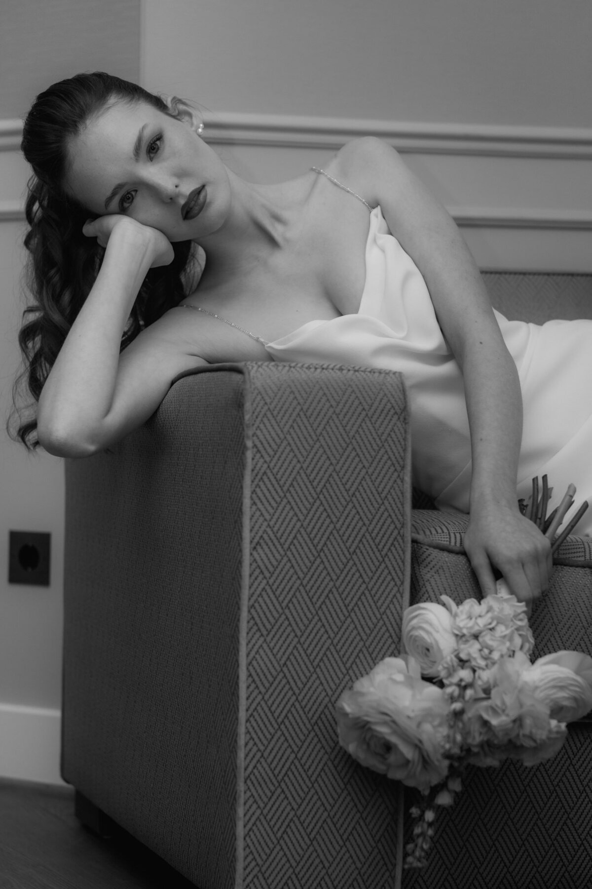 Das Brautmodel liegt den Strauß haltend auf einem Sofa und stützt sich auf eine Hand.
