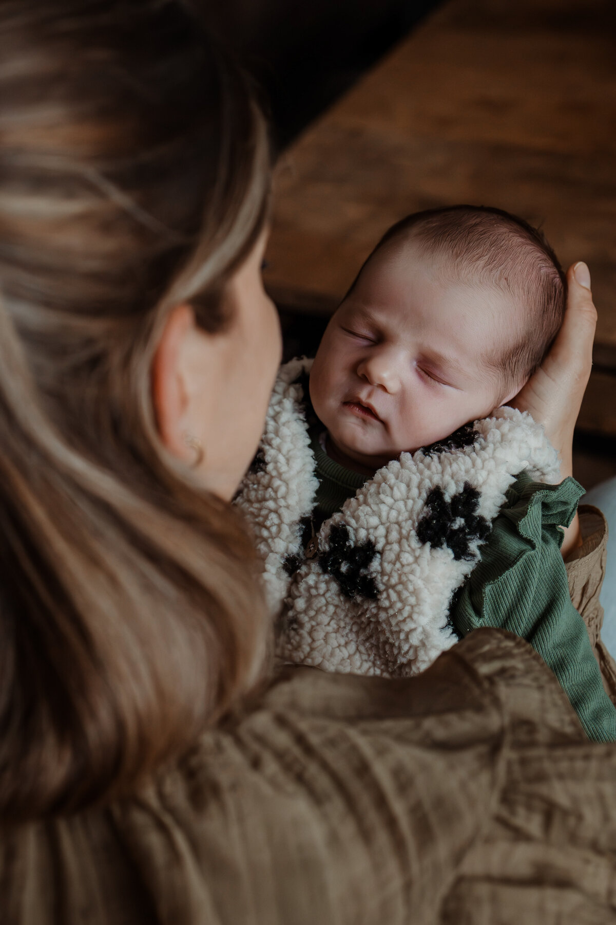 mama houdt haar baby vast, foto over haar schouder zodat je de baby van bovenaf ziet