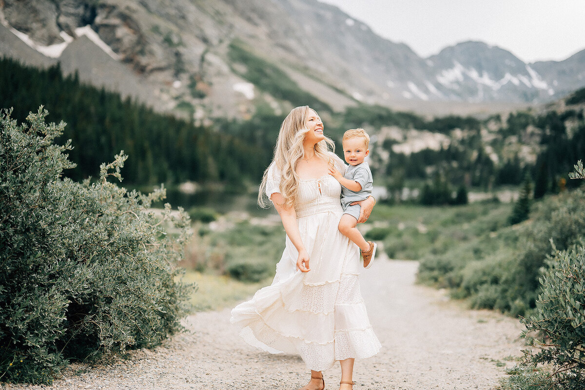 mother holding her son and twirling her dress in front of rocky mountains