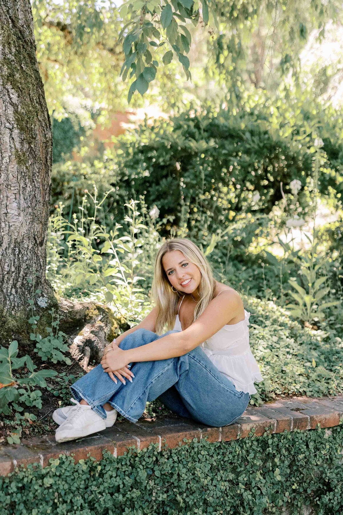 Blonde girl hugging her knees and sitting on a brick wall