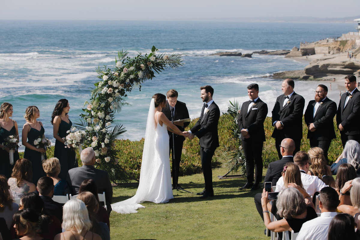 Scenic oceanfront wedding ceremony with floral arch, guests seated overlooking La Jolla coastline.