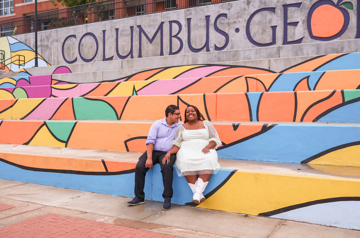 engaged couple sitting in front of  colorful mural with the word Columbus Georgia words