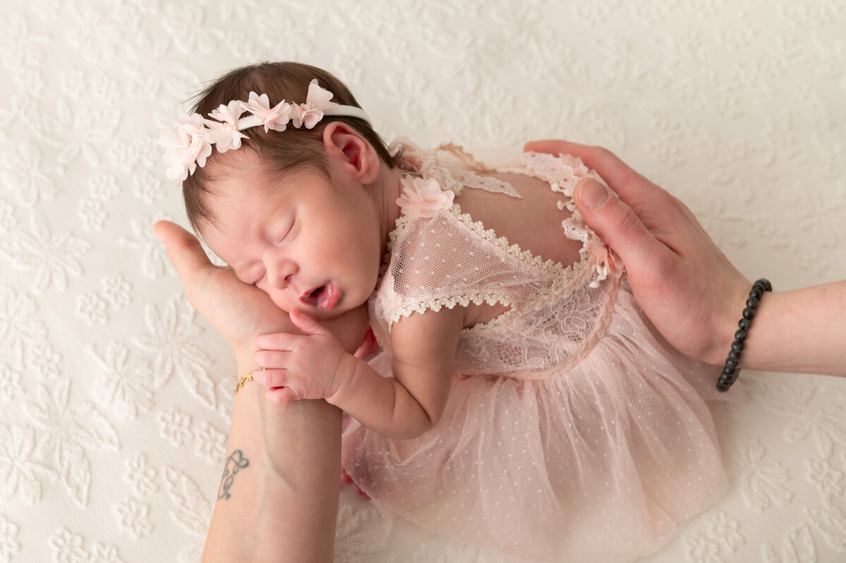 pasgeboren baby meisje in Nelly  Biesemans jurkje gedragen door de handen van mama en papa in een neutrale setting