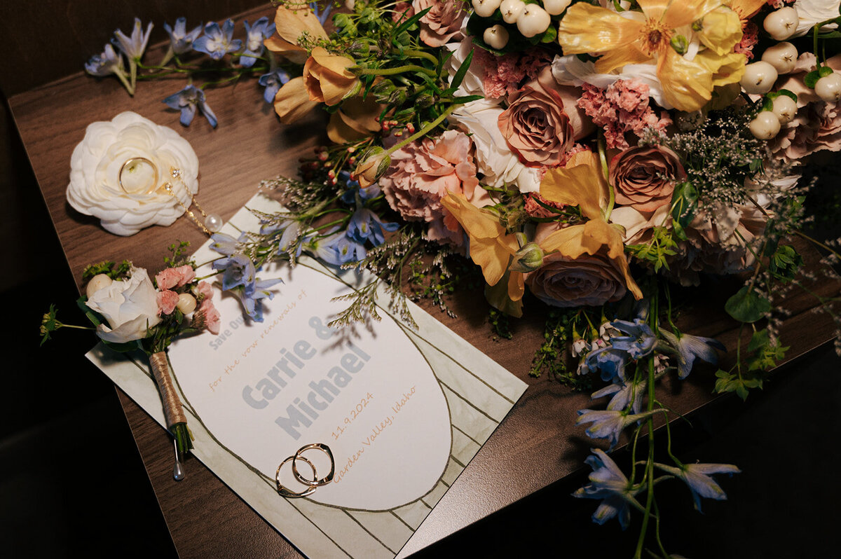 A wedding invitation, rings, flower bouquet and boutonniere.
