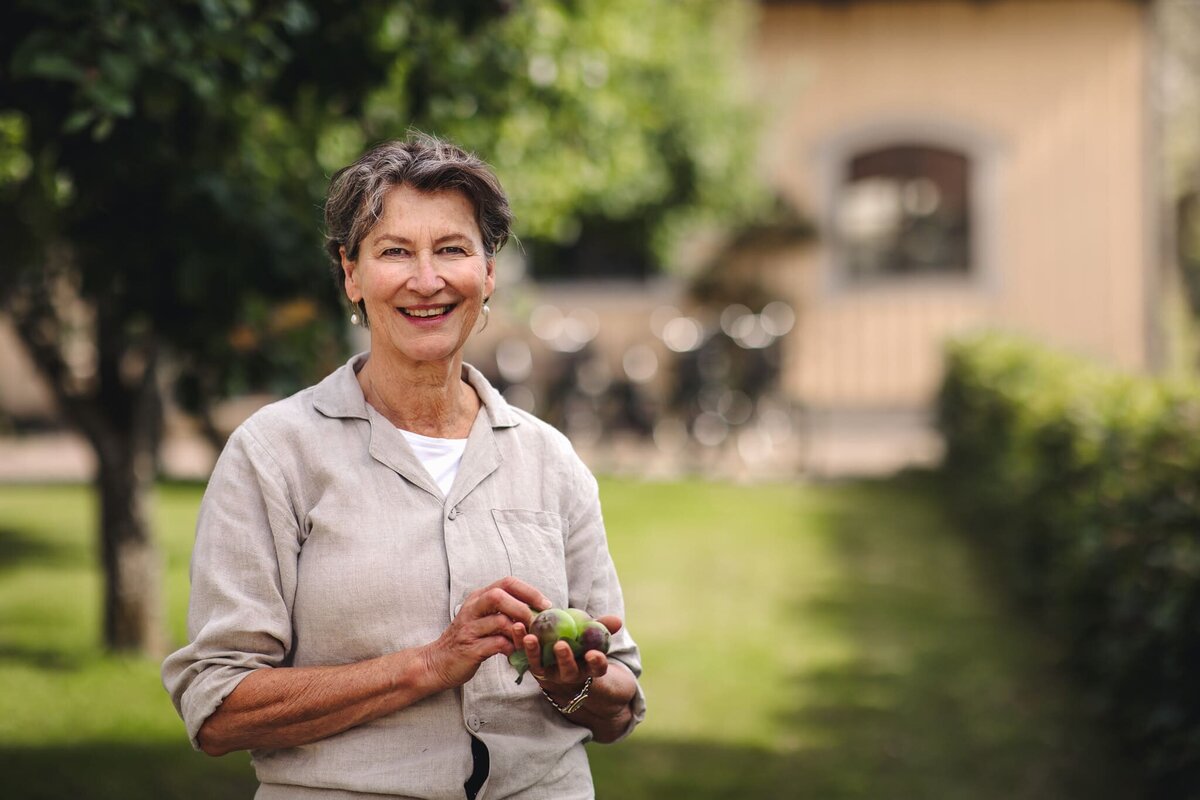 Porträtt av värdinna i trädgårdsmiljö utanför pensionat – verksamhetsfotograf med fokus på storytelling och äkthet.