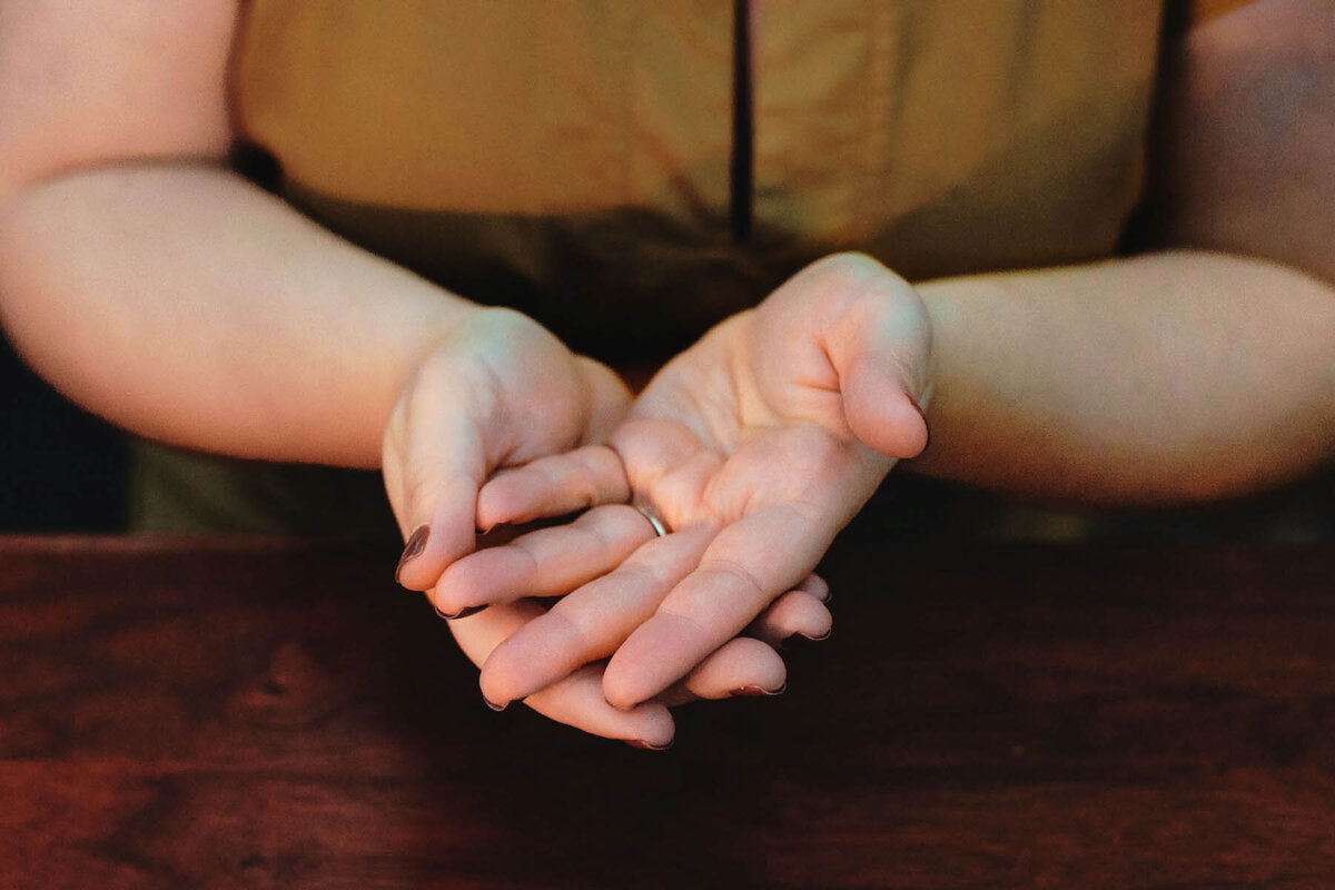 Energy worker Ash Stinson holds out her hands palm up and cupped in each other on a wood table