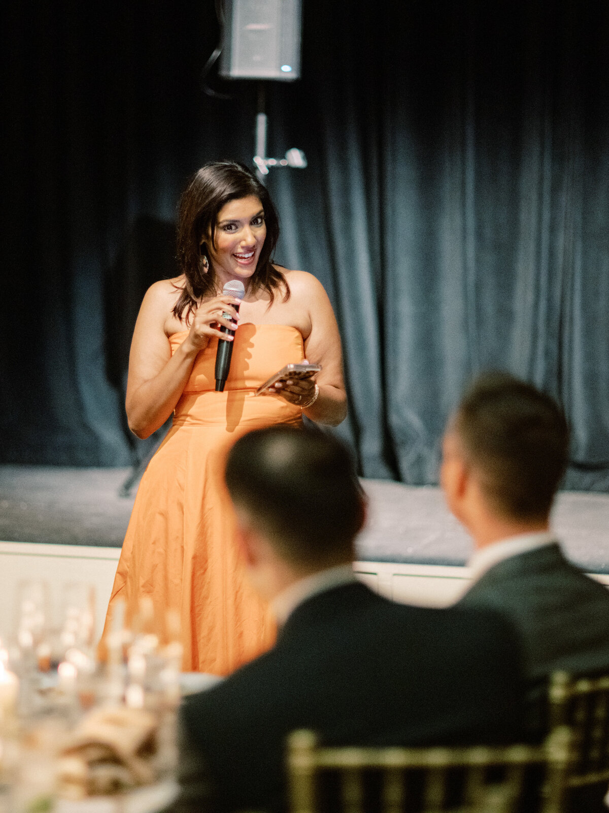 A captivating moment during a wedding reception where a speaker engages the audience, reflecting the warmth and spirit of connection that defines gatherings and fosters memorable experiences.