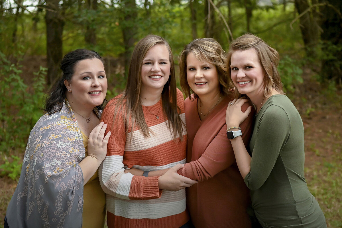 4 women hug each other in a wooded area for their Iowa Family Photographer