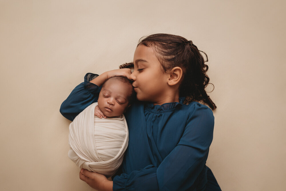 Newborn photos with Atlanta, Georgia newborn photographer of sleeping baby boy with hands under chin wrapped in cream swaddle being held by his big sister.