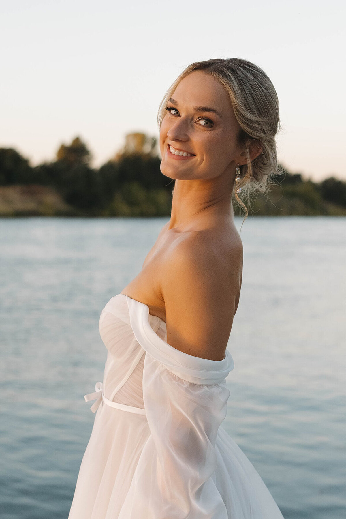 Bride smiling over her shoulder at sunset by the water