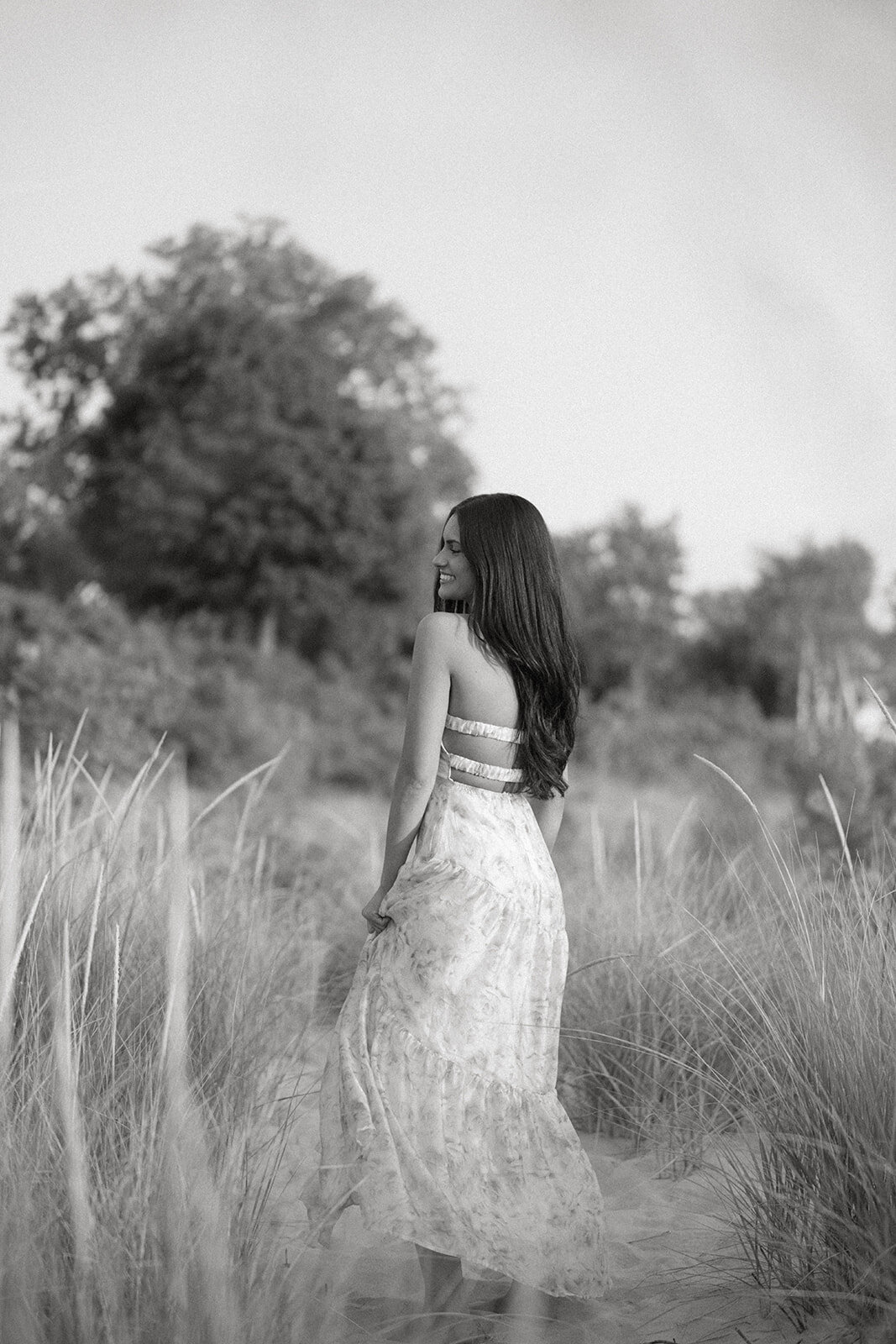 Senior girl looking over her shoulder while walking through dune grass at South Haven North Beach.
