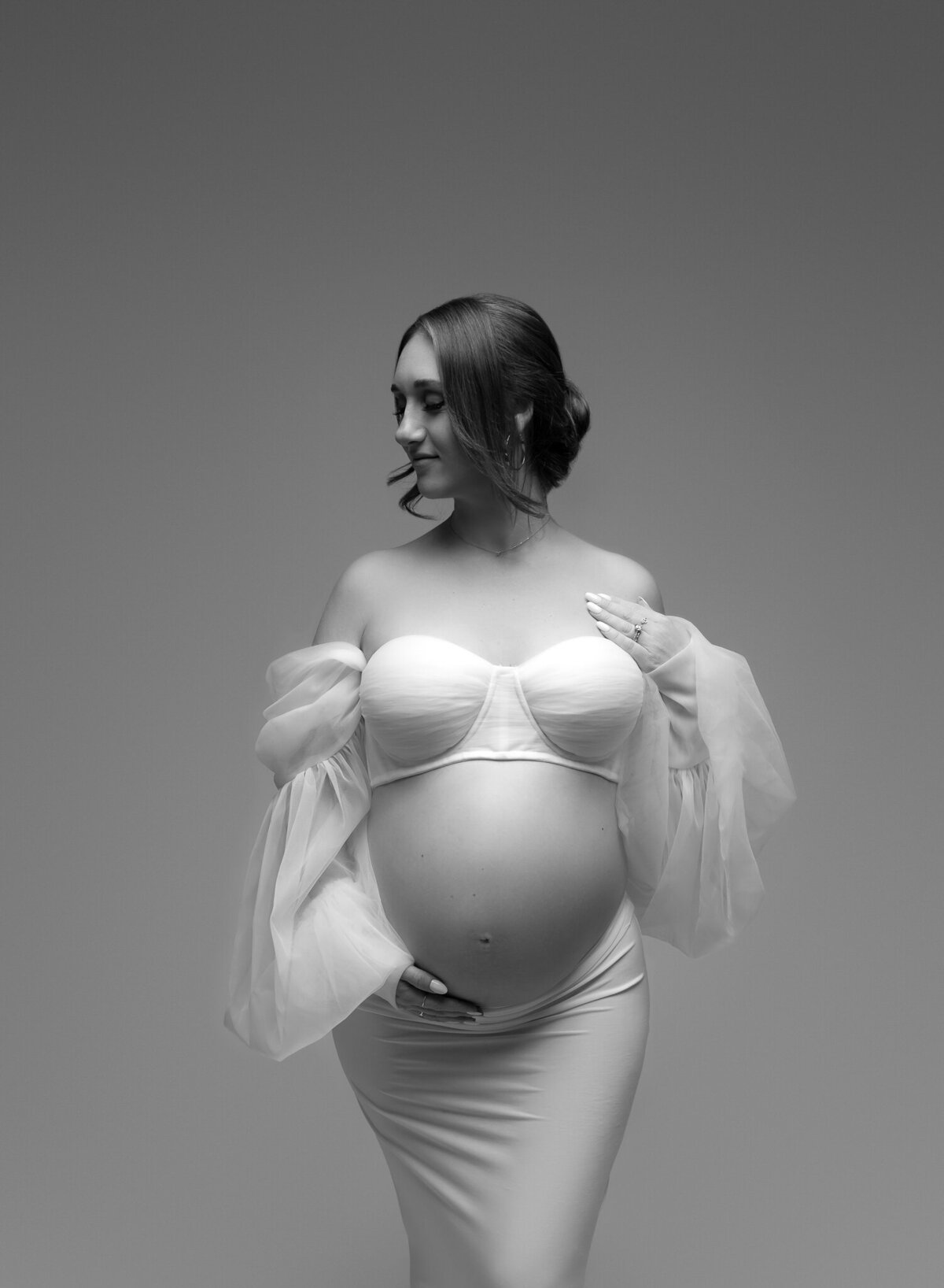 Black and white maternity portrait featuring a sheer-sleeved bustier gown, photographed in a modern Austin studio.