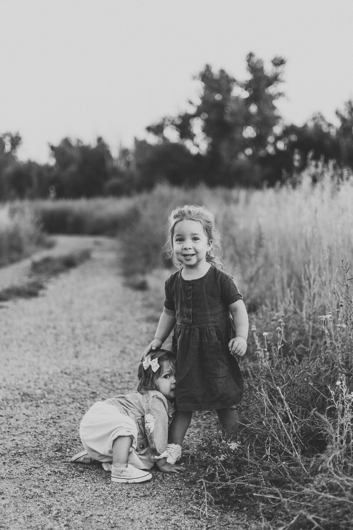 black and white image of two sisters walking on path in field looking at the camera during lifestyle family session in longmont colorado