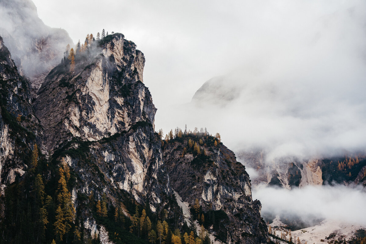 Foggy Dolomites peaks above autumn forest