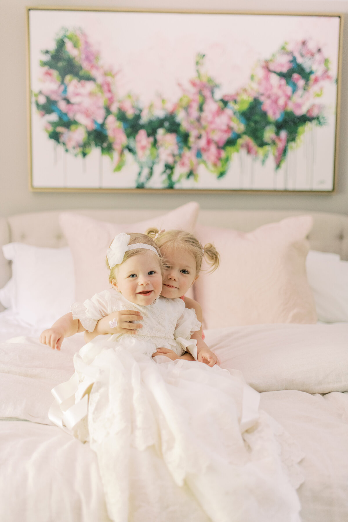 Playful and unposed—baby in a vintage white romper, holding her baptism bonnet with glee. with sister
