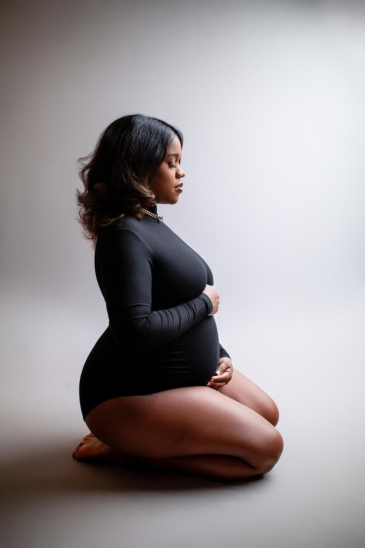 Stunning pregnancy in black body suit on neutral background. Woman looking down at pregnant belly