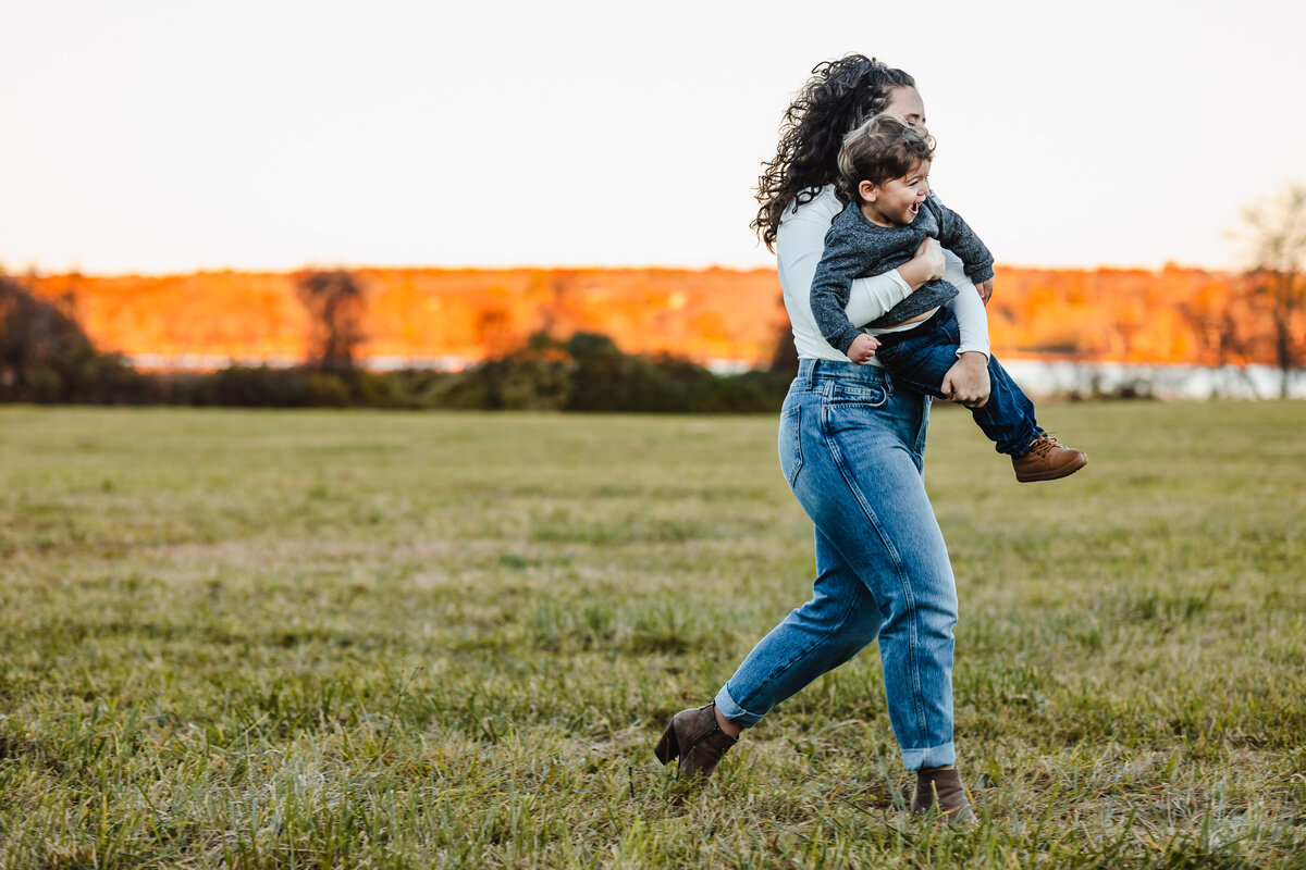 a mom carrying her young son who is smiling through a field