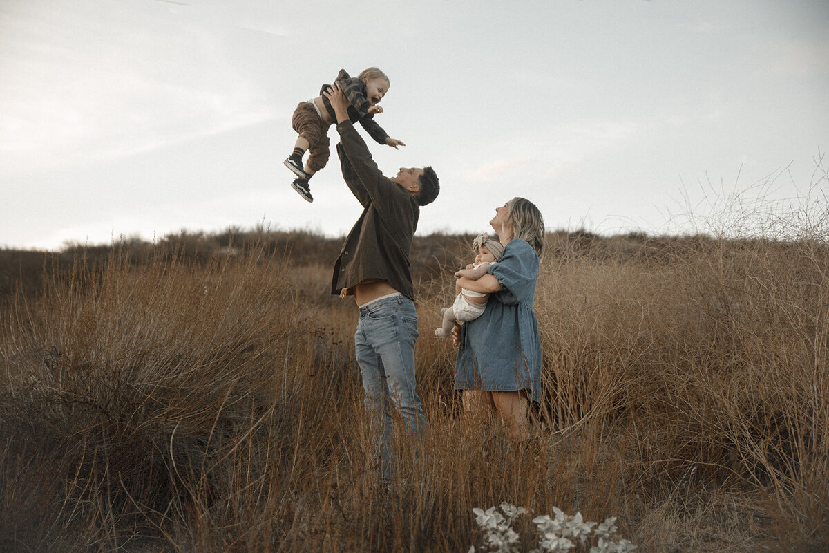 mom and dad play with their two children in field for family photos