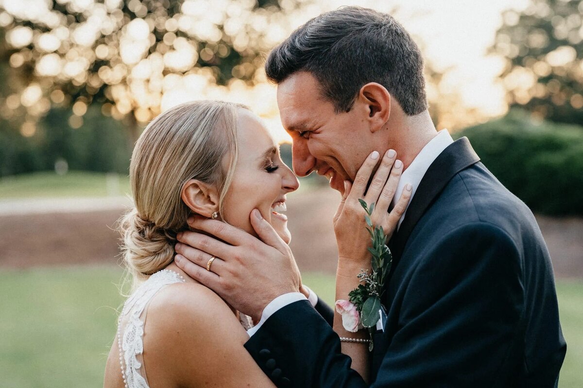 A close-up of a bride and groom laughing together, with the groom gently holding the bride's face