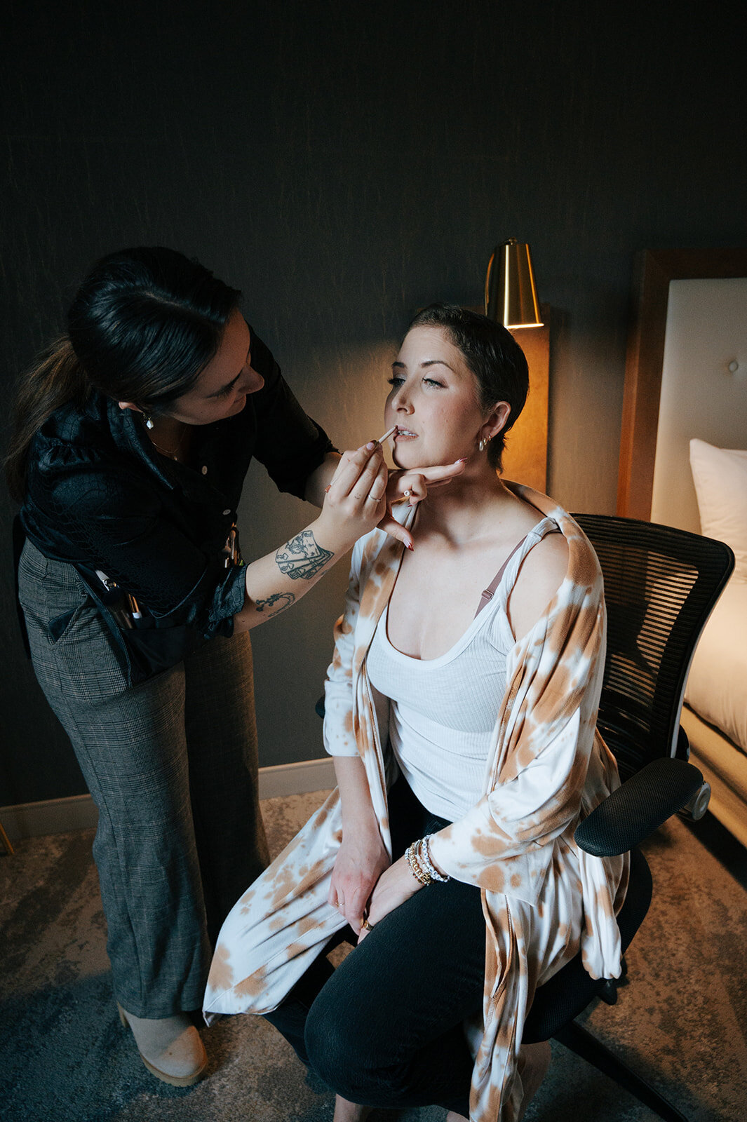 A woman sitting in a chair while a makeup artist applies her makeup.