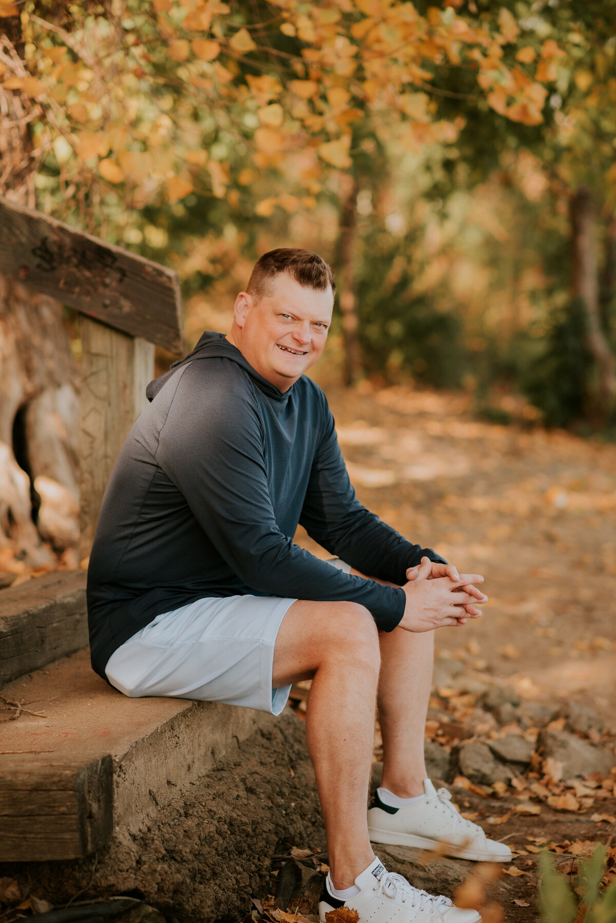 Outdoor dating profile photo of a man seated on a wooded trail in athletic clothing, captured to highlight an active, nature-loving personality for dating apps.